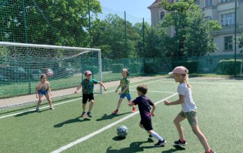 Dzieci bawią się w piłkę na boisku podczas półkolonii aktywnej.